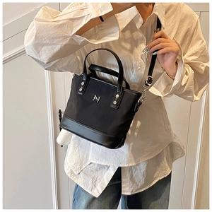 Detail of black canvas and leather bucket bag with silver M1 logo on a female model