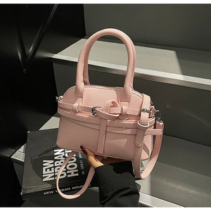 Détail du sac en cuir rose avec boucle argentée et lanières croisées sur livres