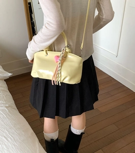 Detail of creamy yellow glossy leather bucket bag with pink heart pendant and woven tassel