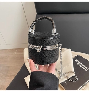 Detail of a mini black quilted cylinder bag with silver buckle and metallic chain strap