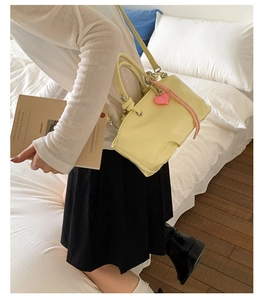 Detail of light yellow leather bucket bag with pink heart charm and adjustable strap