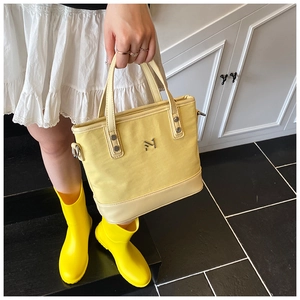 Close-up of yellow canvas tote bag with leather trim and gold M logo on the stairs