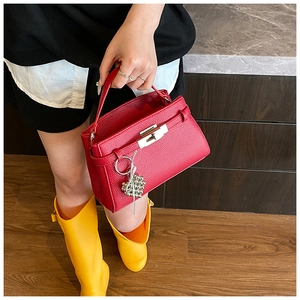 Detail of red pebbled leather handbag with gold metal lock and heart charm accessory