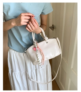 Detail of minimalist cream leather bucket bag featuring cute heart charms and a shoulder strap