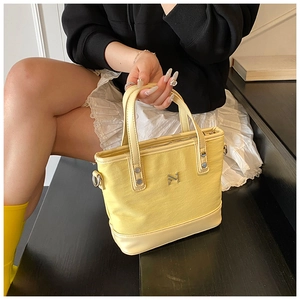 Close-up of the yellow canvas bucket bag showing the silver logo and leather handles
