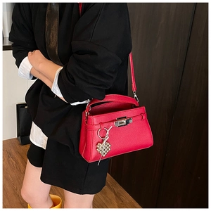 Detail view of a red lychee pattern leather handbag with metallic turn-lock and heart charm