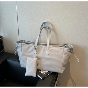 Détail du sac cabas gris tissé avec cordons latéraux et petite pochette sur canapé en cuir