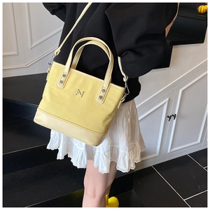 Detail of bright yellow bucket bag with silver metal logo and detachable shoulder strap