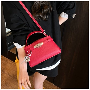 Detail view of red lychee grain leather handbag with gold twist lock and ball charm