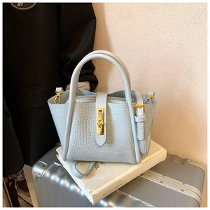 Detail of light blue crocodile texture handbag with gold buckle on a travel suitcase