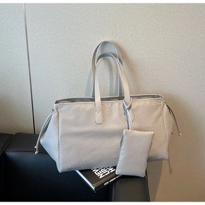 Détail macro du grand cabas tressé gris en cuir avec pochette assortie sur canapé