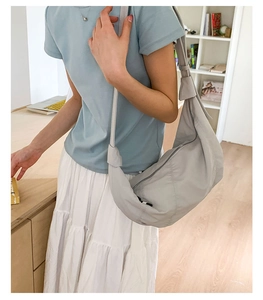 Detail of grey crescent shoulder bag with wide strap and knot design shown on a model