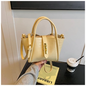 Detail of a creamy yellow crocodile-embossed bucket bag with a golden buckle and handle