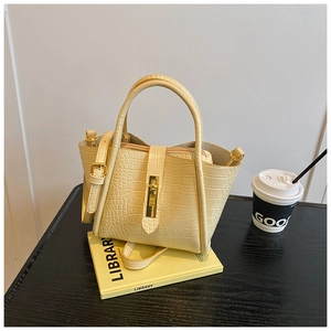 Detail of cream crocodile embossed bucket bag with gold clasp on a wooden desk