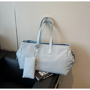 Détail d'un grand sac cabas tissé bleu clair avec mini pochette assortie sur un canapé
