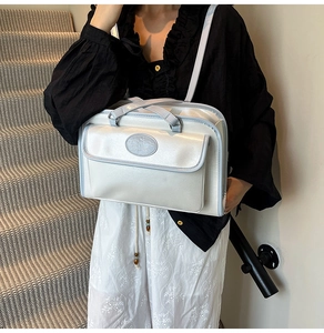 Modèle portant un sac bandoulière blanc perle avec passepoil bleu clair et détails