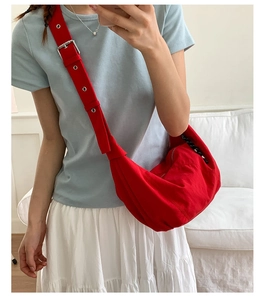 Detail of red nylon dumpling bag featuring wide adjustable strap with metallic eyelets