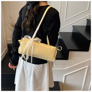 Close-up of cream shoulder bag with white lace bow detail and slim double straps