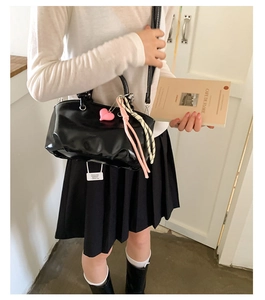 Detailed view of black shiny bucket bag featuring a pink heart charm and braided rope accent