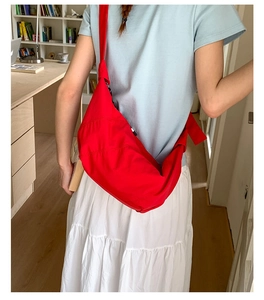 Red nylon canvas crossbody crescent bag shown on model in a casual indoor setting