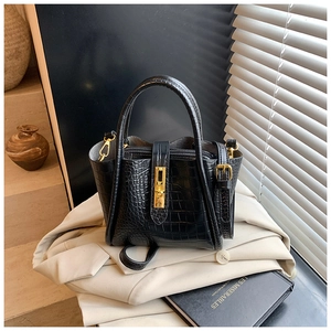 Close-up of black crocodile pattern bucket bag with golden lock on beige blazer