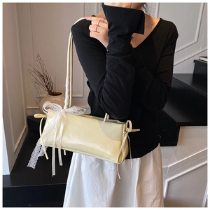 Detail of elegant cream shoulder bag featuring delicate white lace bow and side drawstrings