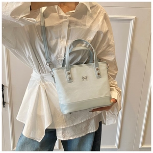 Detail of light blue mini bucket bag with silver M logo and adjustable leather strap
