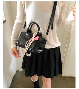 Detail of black patent leather bucket bag with pink heart charm and woven rope handle