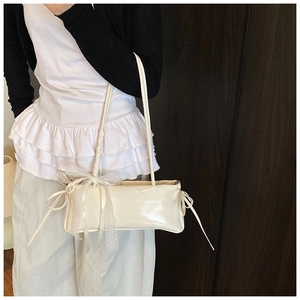 Detail showing the white glossy shoulder bag with lace trim and delicate ribbon bow accent