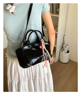 Detail view of glossy black mini bucket bag with heart pendant and thin shoulder strap