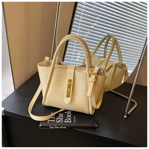 Detail of cream faux crocodile bucket bag with gold hardware on a reflective mirror