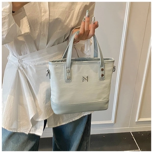 Detail of light blue faux leather bucket bag showing silver metal logo and handle texture