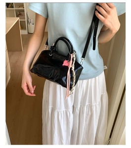 Detail of glossy black leather bucket bag featuring pink heart charm and braided strap