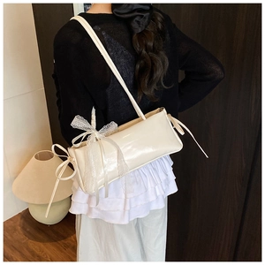 Detail of creamy white patent leather shoulder bag featuring delicate lace bow decoration