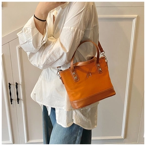 Detail of orange canvas and leather bucket bag with metallic logo and gold hardware studs