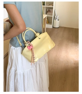 Detailed shot of cream yellow leather bucket bag with pink heart charm shown on model