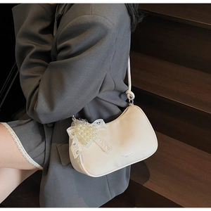 Dettaglio della borsa hobo bianca con fiocco in pizzo e ciondolo a cuore di perle