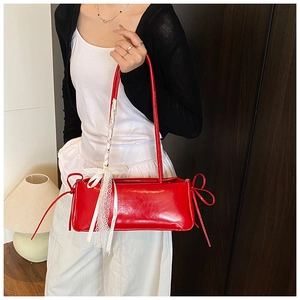 Close-up of a red patent leather shoulder bag with side bows and lace ribbon detail