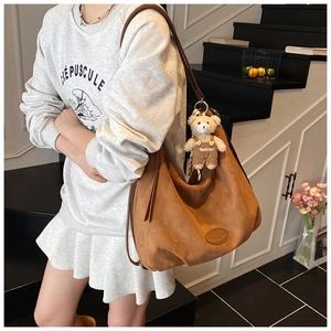Detail of a brown suede tote bag with a cute teddy bear charm in a lifestyle setting