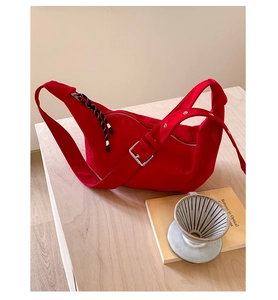 Detail of red crescent nylon crossbody bag with metal buckle on light wood desk