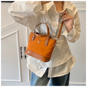 Model wearing a stylish orange canvas bucket bag with metallic M logo and strap