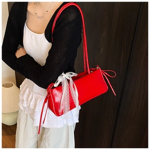 Detail of red glossy shoulder bag featuring white lace bow and side drawstring ruching
