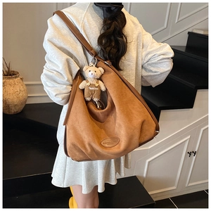 Brown faux suede hobo bag with teddy bear pendant shown on a shoulder in detail