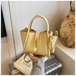 Close-up of cream faux leather bucket bag with crocodile texture and gold lock hardware