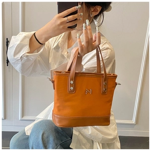 Detail of orange canvas bucket bag with brown leather handles and metal lettering