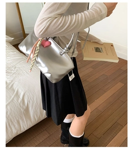 Detailed side view of a metallic silver bucket bag with pink heart charm and silk scarf