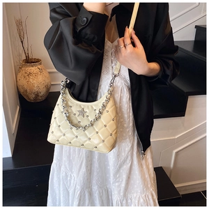 Detail shot of a quilted cream shoulder bag with silver star emblem and metal chain strap