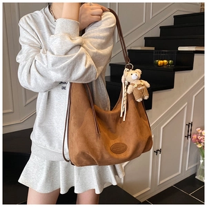 Detail of a brown suede hobo bag with adjustable strap and decorative bear charm