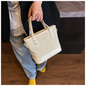 Detail of elegant cream bucket bag featuring silver M-shaped logo and sturdy leather handle