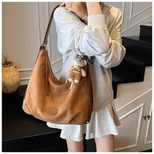 Detail of a brown suede Hobo tote bag with fashion label and cute plush bear charm